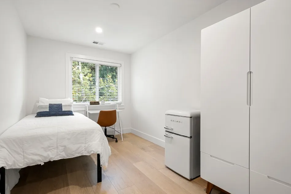 Bright and cozy bedroom with a minimalist design, featuring a single bed, a sleek desk by the window, and ample natural light.