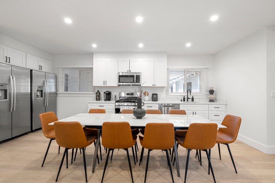 Bright, modern kitchen and dining area featuring sleek white cabinetry, stainless steel appliances, and a spacious table.