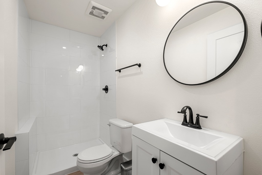 Modern bathroom with sleek white tiles, a stylish round mirror, and elegant black fixtures.