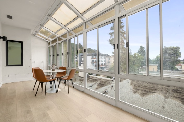 Bright sunroom with large windows offering scenic views, featuring a sleek dining table and modern chairs.