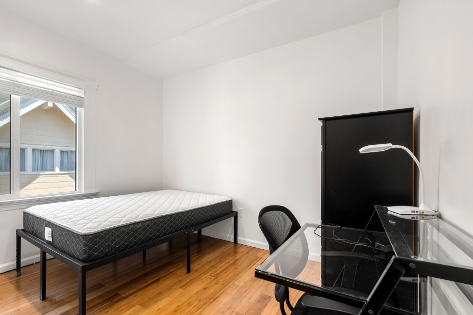 Bright and modern bedroom with a comfortable single bed, minimalist desk setup, and large window for natural light.