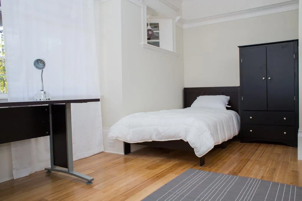 Bright and cozy bedroom with a single bed, modern desk, and sleek wardrobe, all accented with warm wooden flooring.