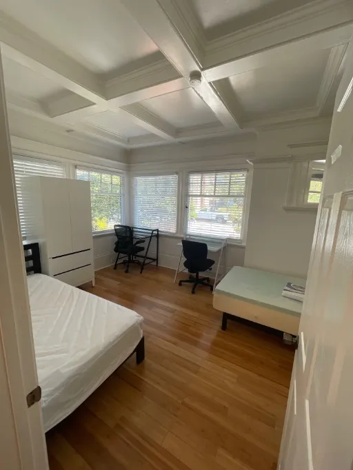 Bright and cozy bedroom with natural light, featuring wooden floors, a comfortable bed, a wardrobe, and a compact study area with a desk and chair.