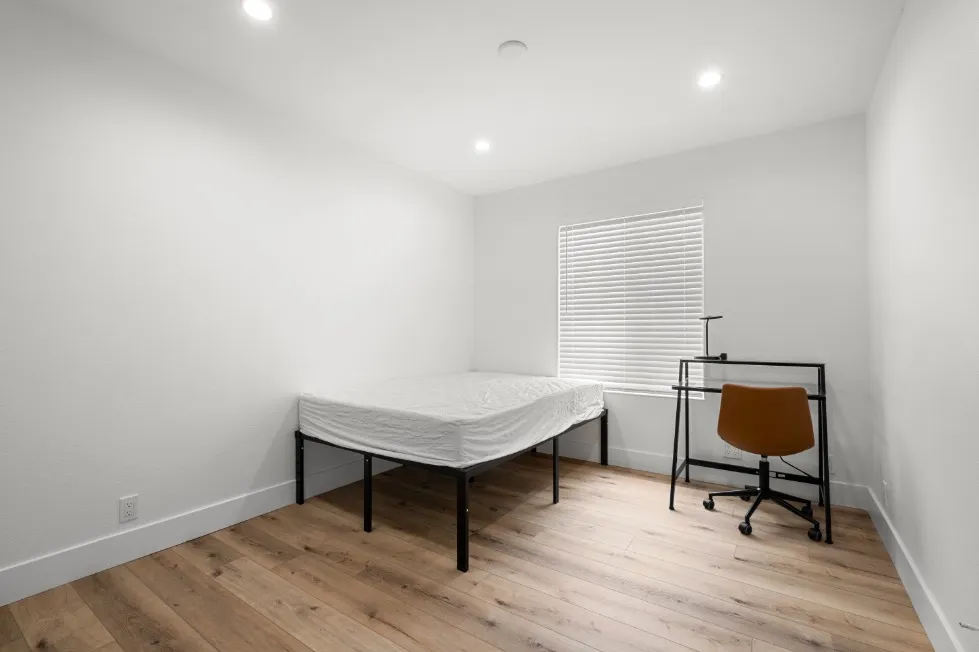 Bright minimalist bedroom featuring modern hardwood floors, a cozy bed, and a stylish desk chair set by the window.