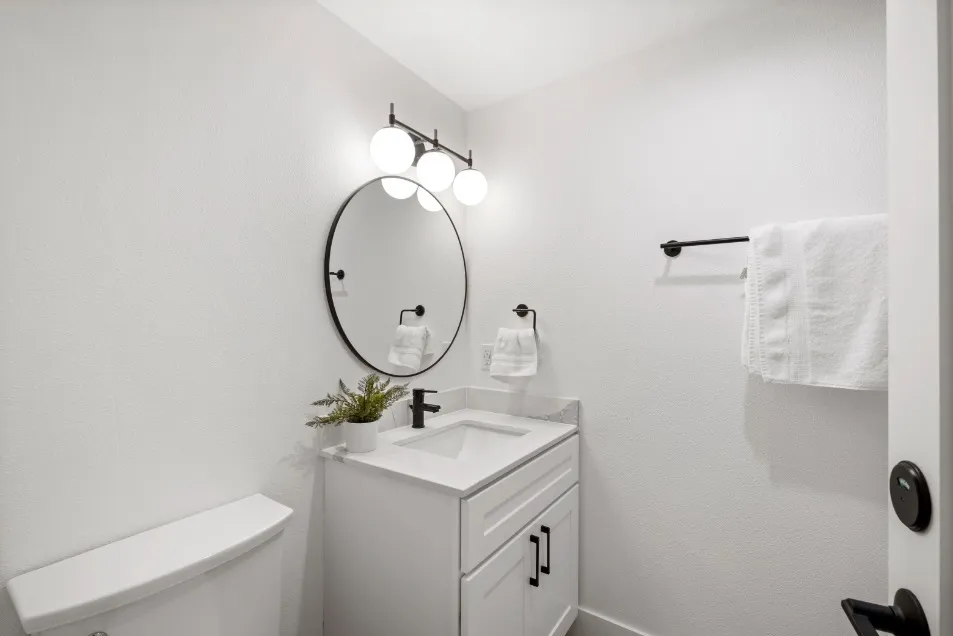 Modern bathroom with sleek white vanity, round mirror, and stylish lighting.