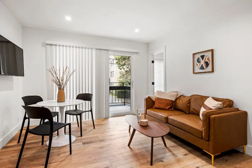 Modern living room with stylish furnishings, featuring a cozy brown sofa, sleek round dining table, and balcony access for natural light.