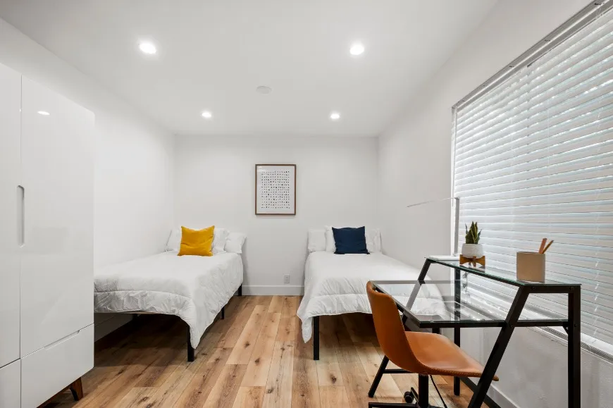 Bright and modern bedroom with twin beds, natural light, and a sleek study desk.