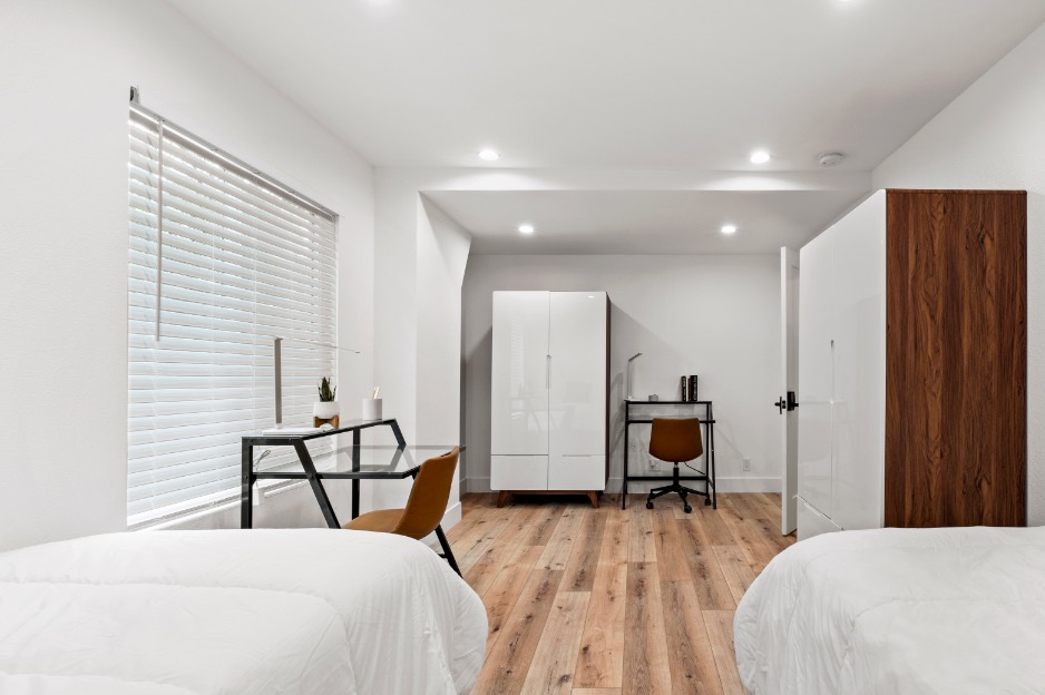 Bright and modern bedroom with stylish hardwood flooring, twin beds, cozy workspace, and ample storage.