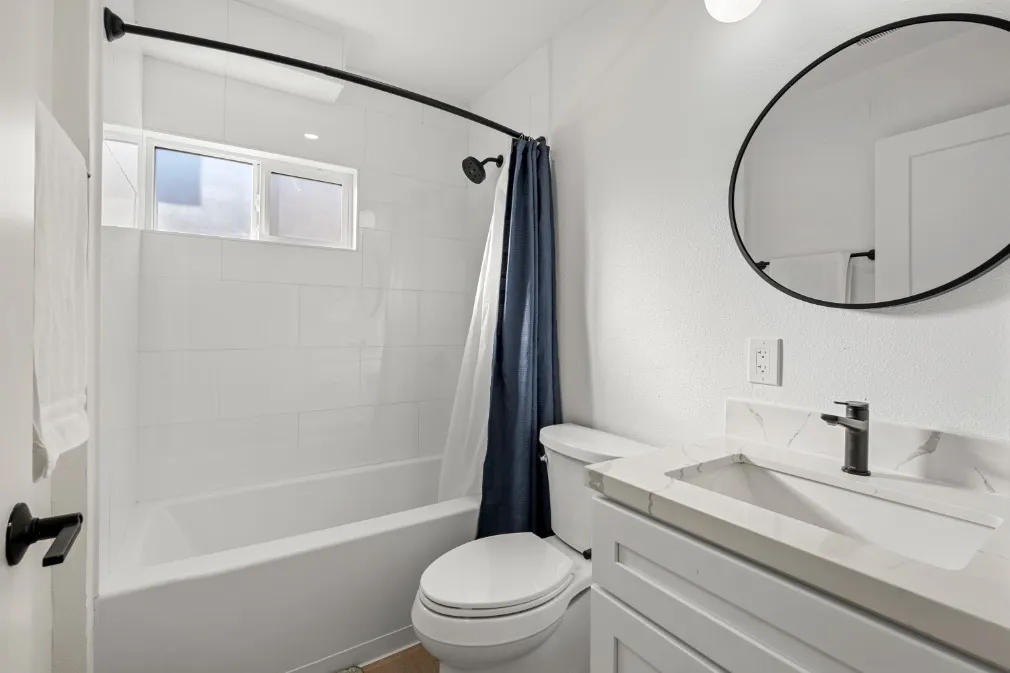 Bright and modern bathroom featuring a sleek vanity, elegant round mirror, and a shower.