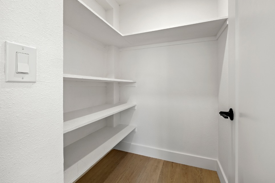 Bright walk-in closet with built-in white shelving and sleek modern door.