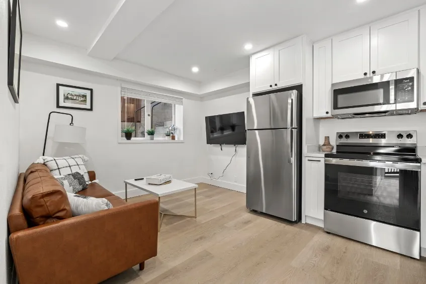 Modern open-plan living area with stylish kitchen, stainless steel appliances, cozy brown leather sofa, and bright decor.