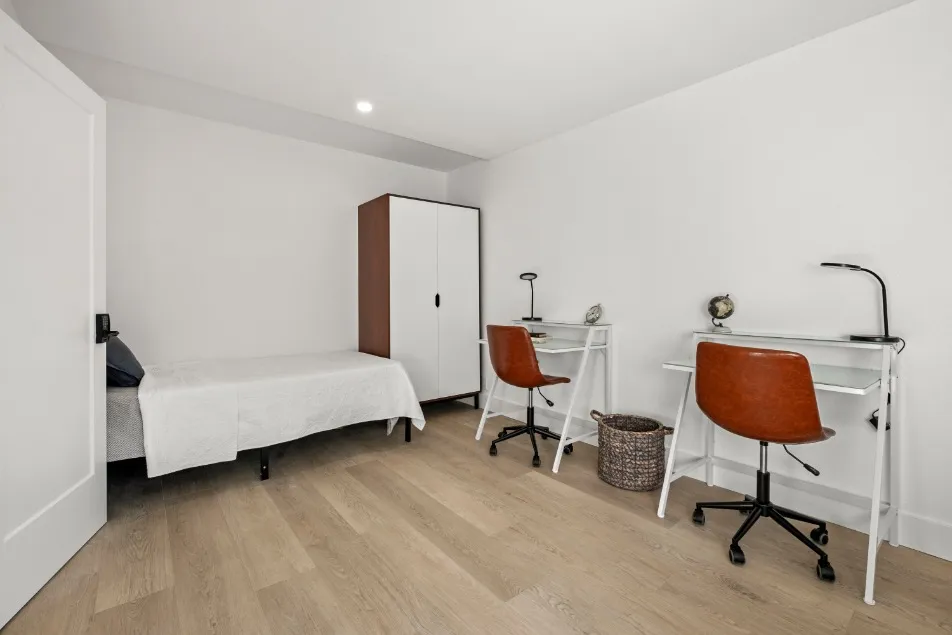 Contemporary bedroom featuring a minimalist design with two sleek workstations, a cozy bed, and stylish wooden flooring.