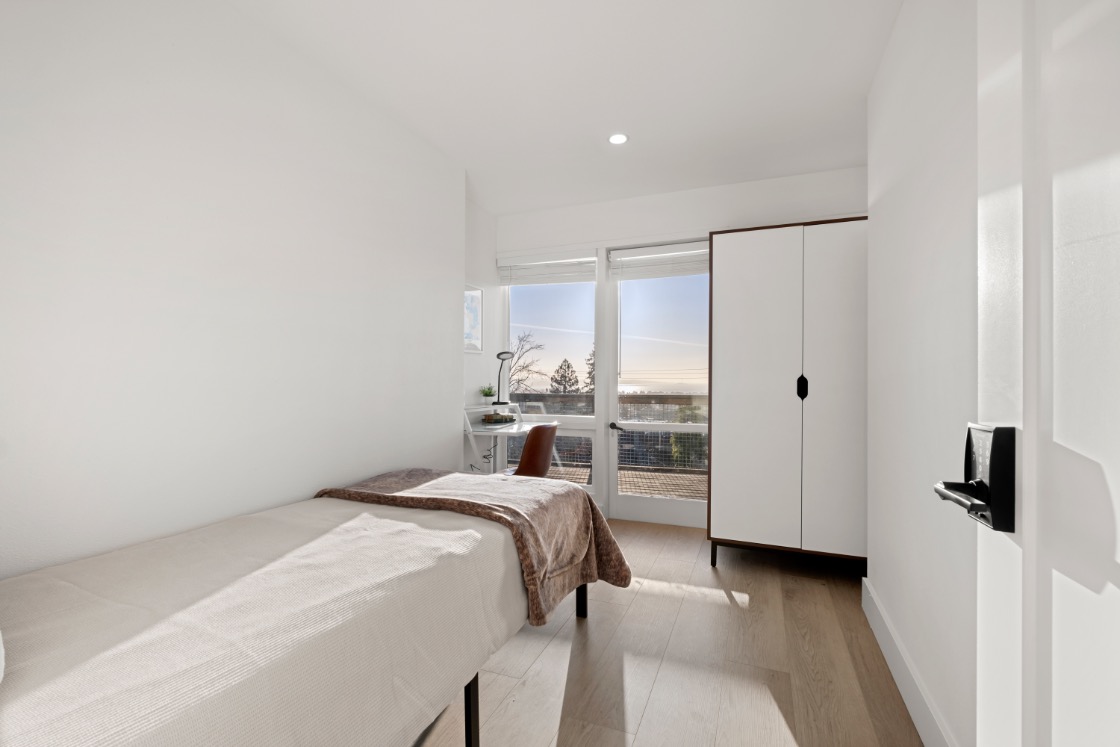 Bright, minimalist bedroom with elegant finishes, large window offering a serene view, and ample storage space.