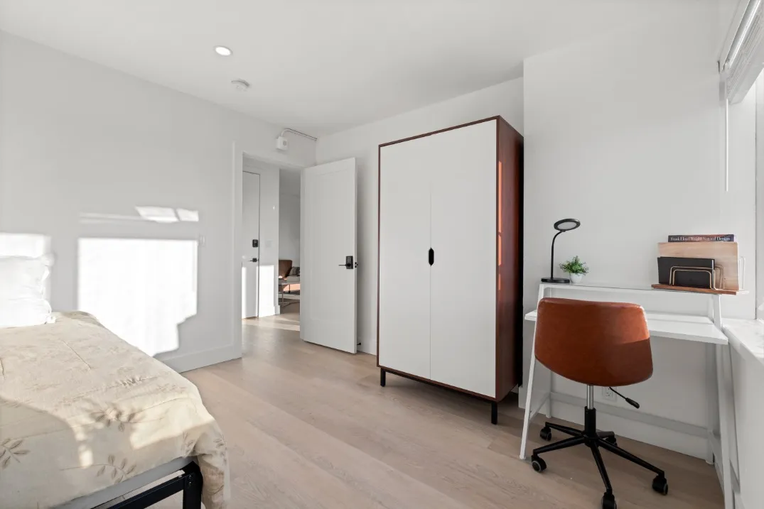 Bright and inviting bedroom featuring a cozy bed, sleek white wardrobe, and a modern workspace with a stylish chair.