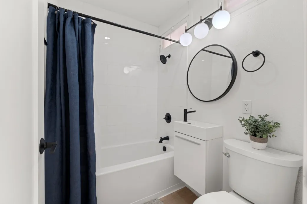 Modern bathroom featuring a sleek white vanity, circular mirror, and blue shower curtain.