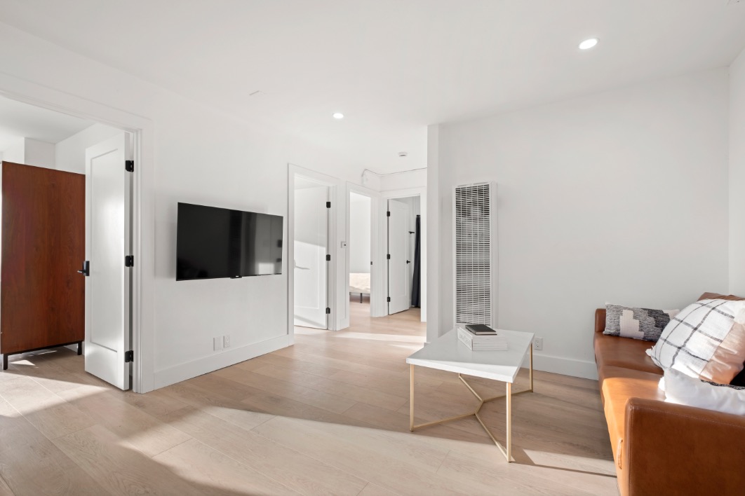 Modern living room with sleek decor, featuring a cozy brown leather couch, wall-mounted TV, and elegant white coffee table in a bright, open space.