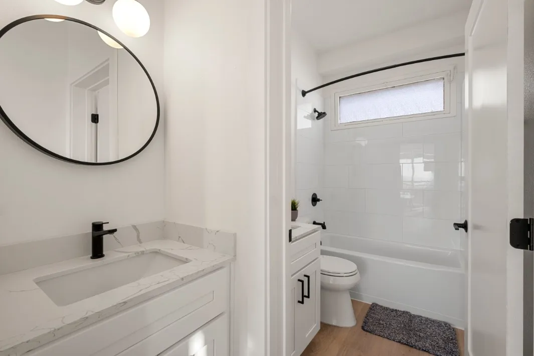 Sleek modern bathroom featuring a marble countertop, oval mirror, and stylish fixtures with a pristine bathtub.