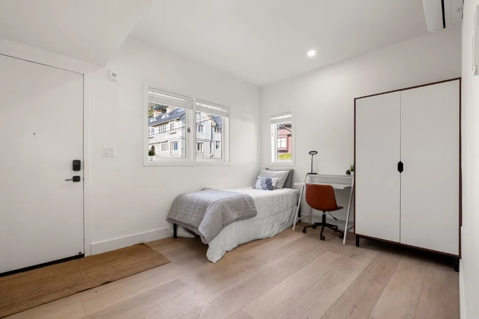 Cozy bedroom with a single bed, modern wardrobe, and study desk in a bright, airy space with wooden flooring.