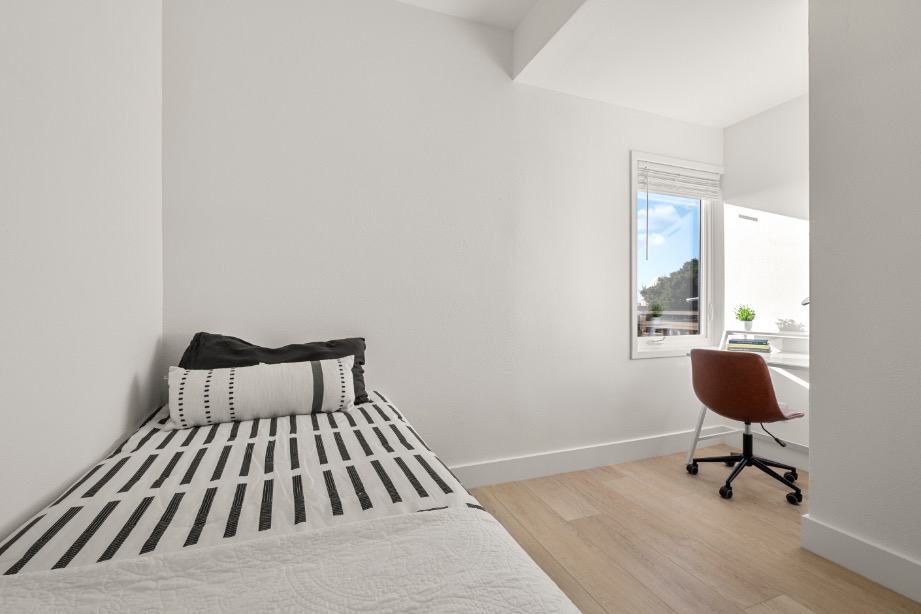 Cozy bedroom corner with a single bed, modern striped bedding, and a bright workspace by the window.