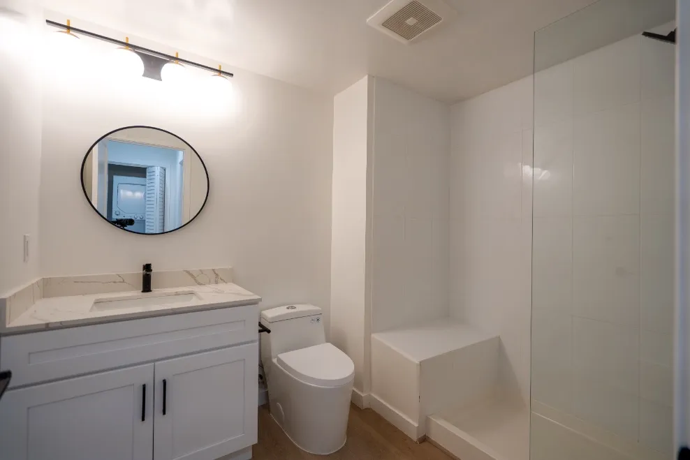 Modern bathroom with sleek white vanity, large mirror, and spacious walk-in shower.