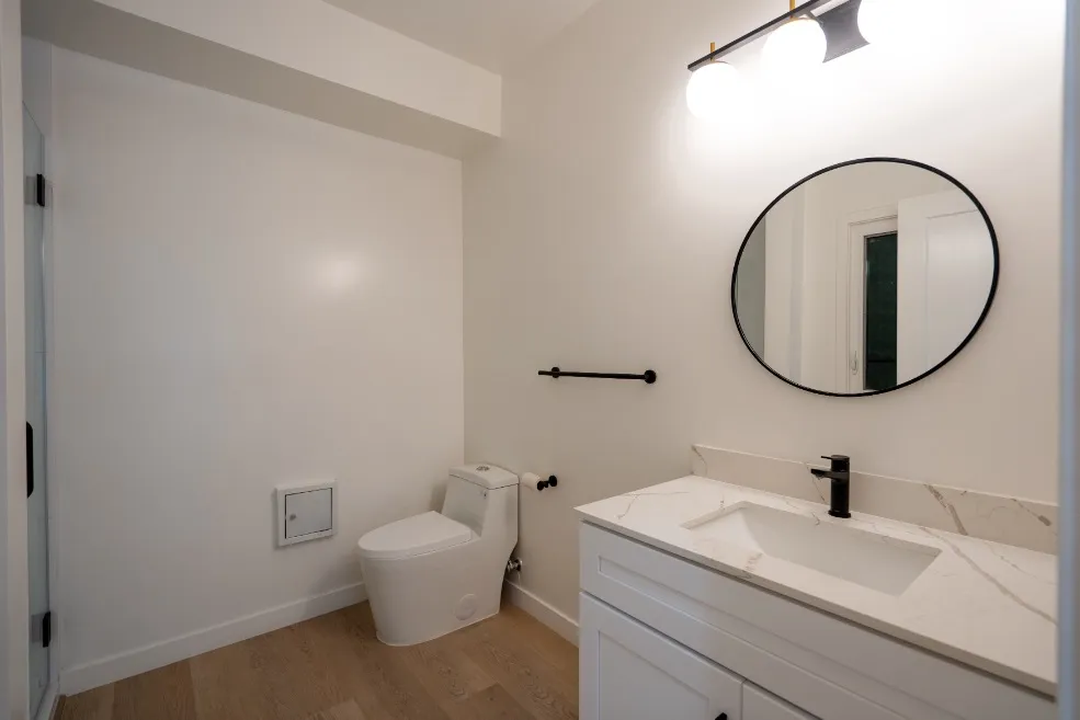 Elegant bathroom featuring a modern vanity with a marble countertop, stylish round mirror, and contemporary light fixtures.