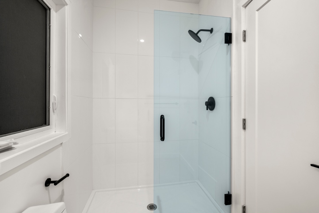 Modern bathroom with sleek glass shower enclosure, white tiles, and stylish matte black fixtures.