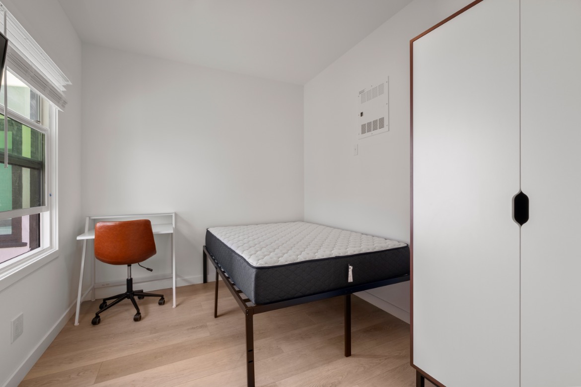Bright and cozy bedroom with modern desk, comfy chair, and sleek wardrobe.
