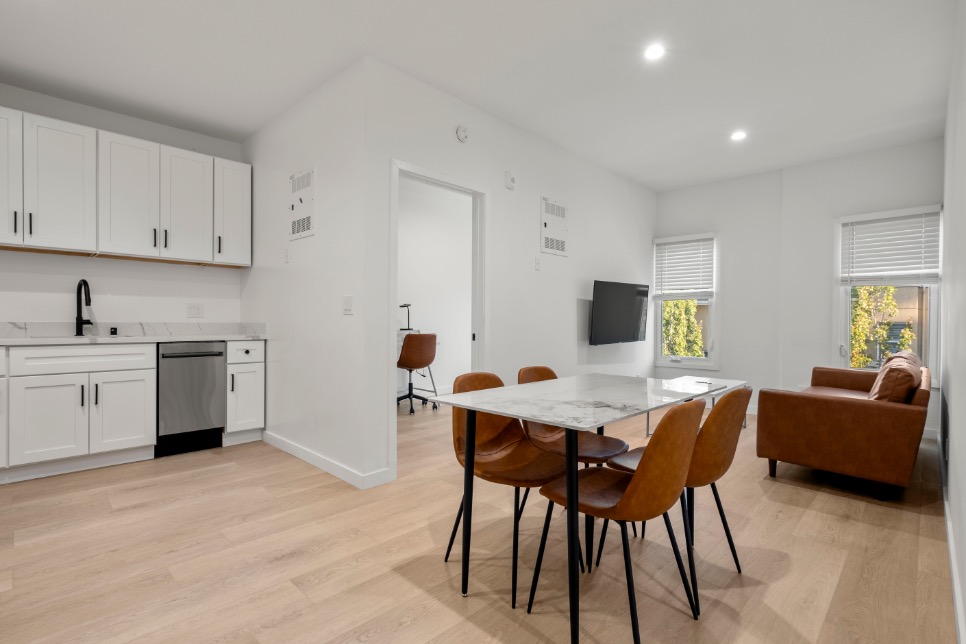 Modern open-concept dining and living area featuring stylish furnishings and a sleek kitchen with white cabinetry and stainless steel appliances.
