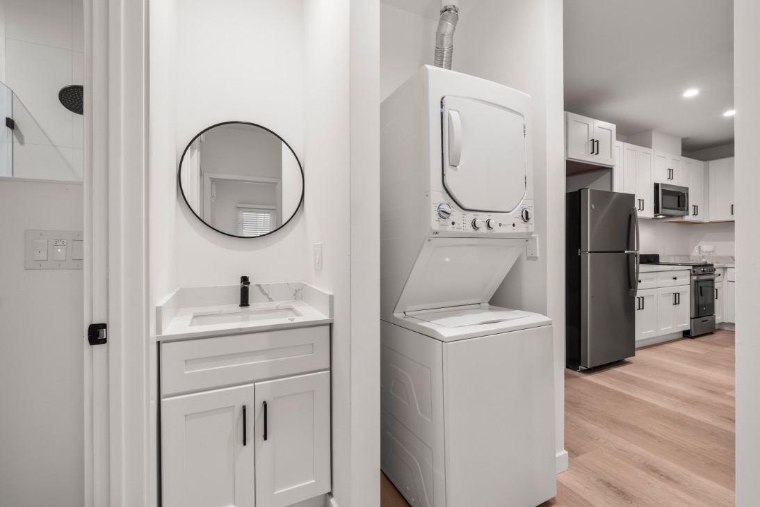 Elegant apartment interior showcasing a sleek washer and dryer unit adjacent to a modern kitchen with stainless steel appliances and white cabinetry.