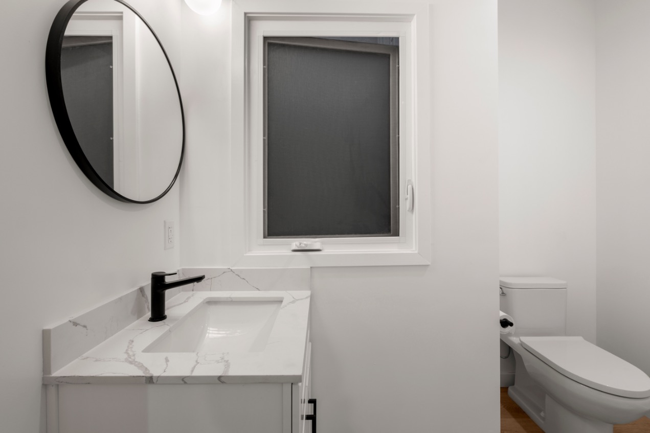 Modern bathroom with sleek white fixtures, elegant marble countertop, and round mirror for a sophisticated touch.