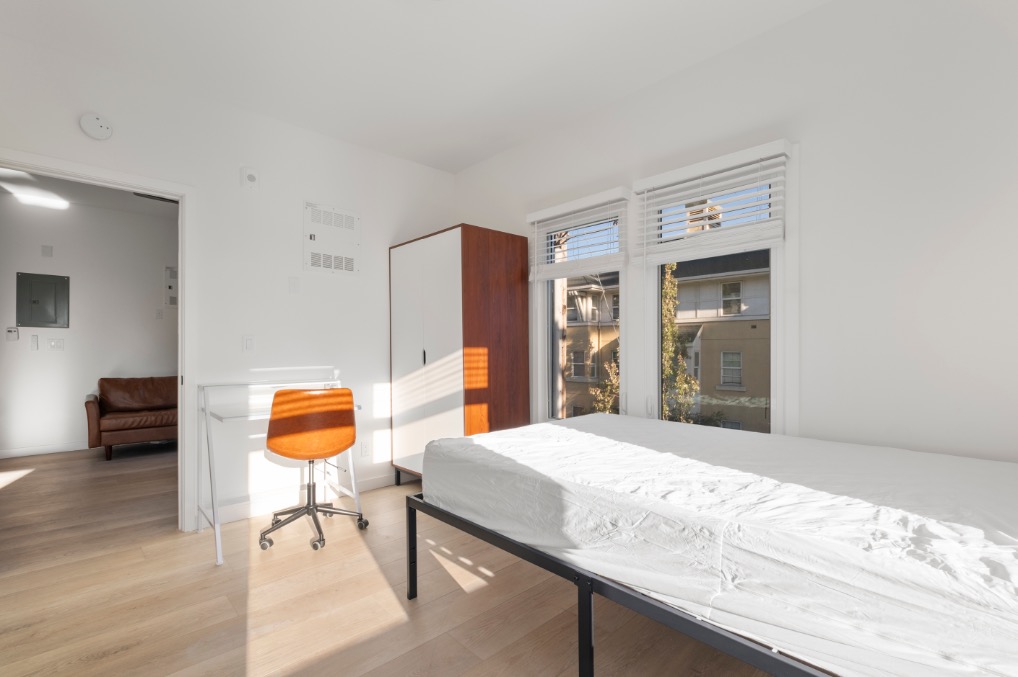 Bright bedroom with large windows, modern wooden flooring, and sleek furnishings including a work desk and chair.
