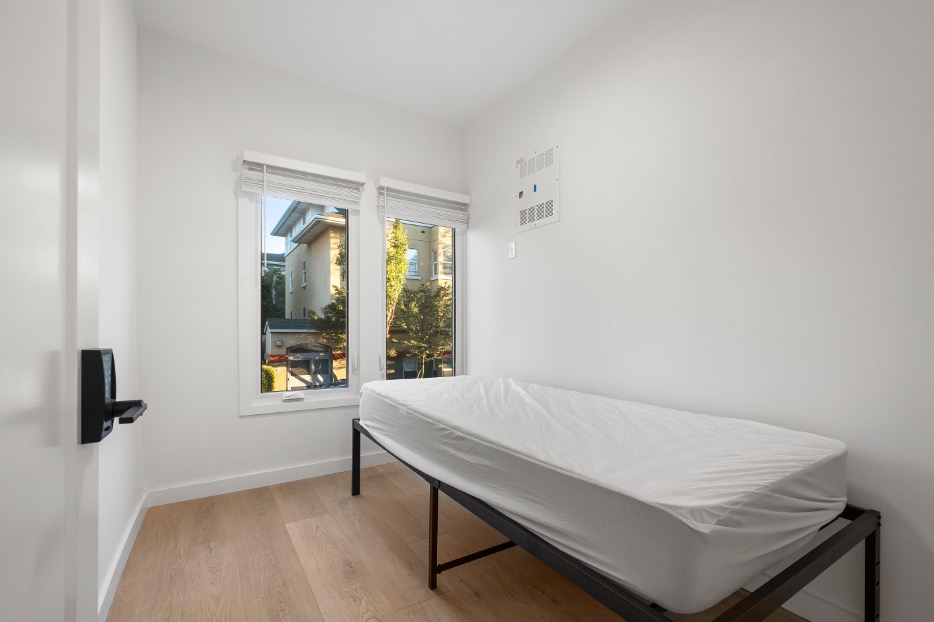 Bright and cozy bedroom with a single bed, large windows, and natural light overlooking a charming neighborhood view.