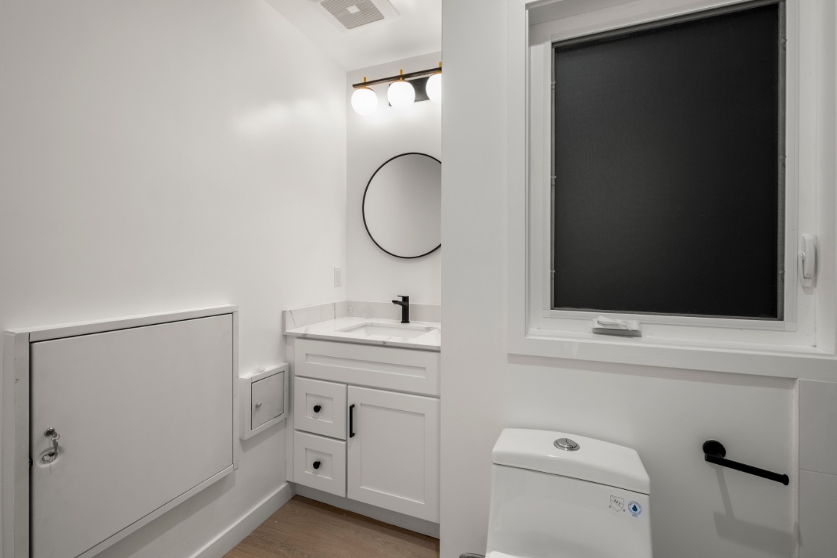 Sleek modern bathroom with white cabinetry, circular mirror, and soft lighting.