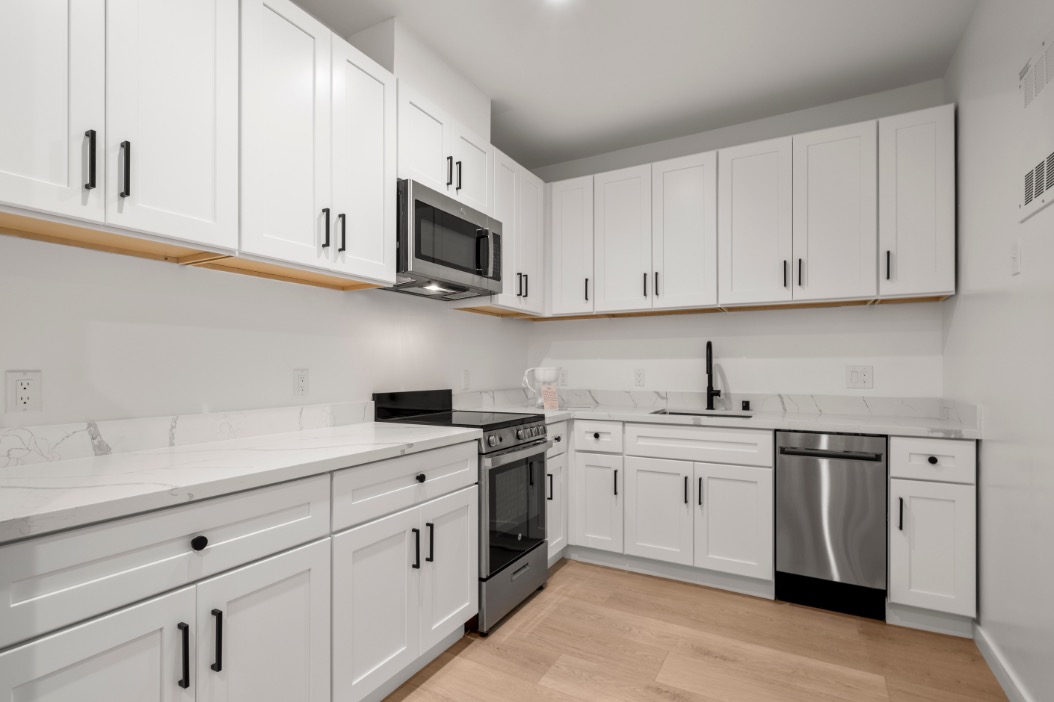 Modern kitchen featuring sleek white cabinetry, stainless steel appliances, and elegant marble countertops with ample space.