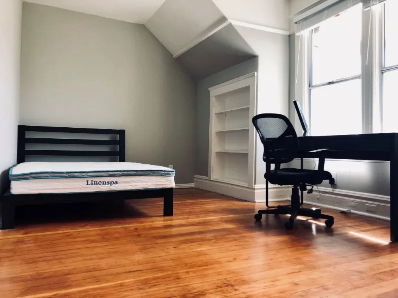 Bright and airy bedroom featuring a sleek desk, comfortable bed, and natural wood flooring.