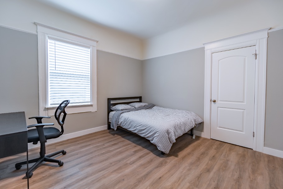 Bright and inviting bedroom with modern decor, featuring a comfortable bed, sleek desk, and ergonomic chair on elegant wood flooring.