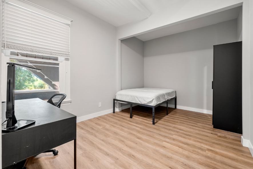 Bright, minimalist bedroom with modern furnishings, featuring a large window, sleek desk, and comfortable bed.