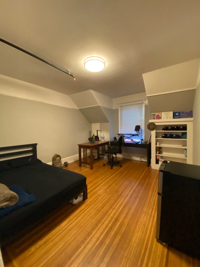 Cozy bedroom with sleek wooden floors, a spacious desk, modern lighting, and ample shelving offering a comfortable living space.