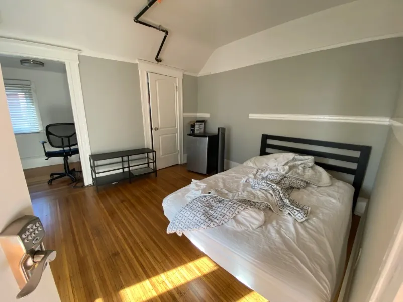 Cozy bedroom with modern furniture, featuring a comfy double bed and workspace, enhanced by natural light and elegant hardwood flooring.