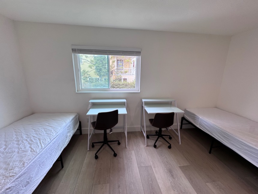 Bright dual-bedroom setup with two beds, desks, and a scenic window view.