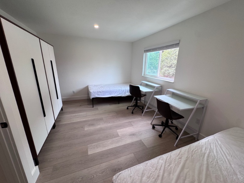 Bright, modern bedroom with two workstations, large wardrobe, and serene outdoor view.
