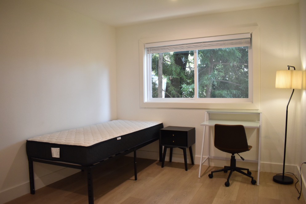 Bright and cozy bedroom with a single bed, modern desk, and chair set against a large window with a serene outdoor view.