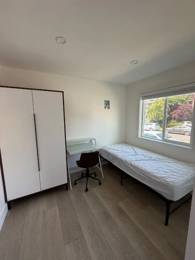 Bright and cozy bedroom with a single bed, large wardrobe, and a study nook featuring a desk and chair, all bathed in natural light from a generous window.