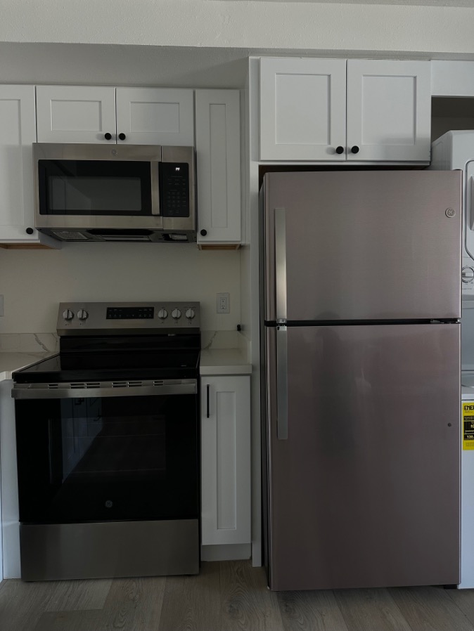 Modern kitchen with sleek stainless steel appliances, including a microwave, oven, and fridge, complemented by elegant white cabinetry.