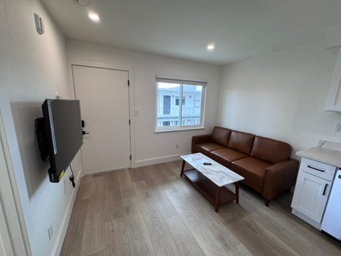 Inviting modern living room with sleek hardwood floors, cozy brown leather sofa, and a large window for natural light.