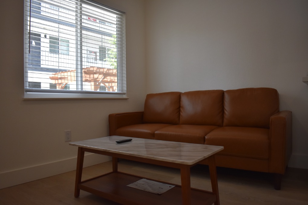 Inviting living room with a sleek brown leather sofa and elegant marble coffee table, bathed in natural light through large window blinds.