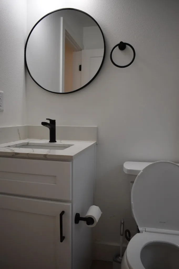 Elegant modern bathroom featuring a sleek white vanity with marble countertop, round mirror, and stylish black fixtures.