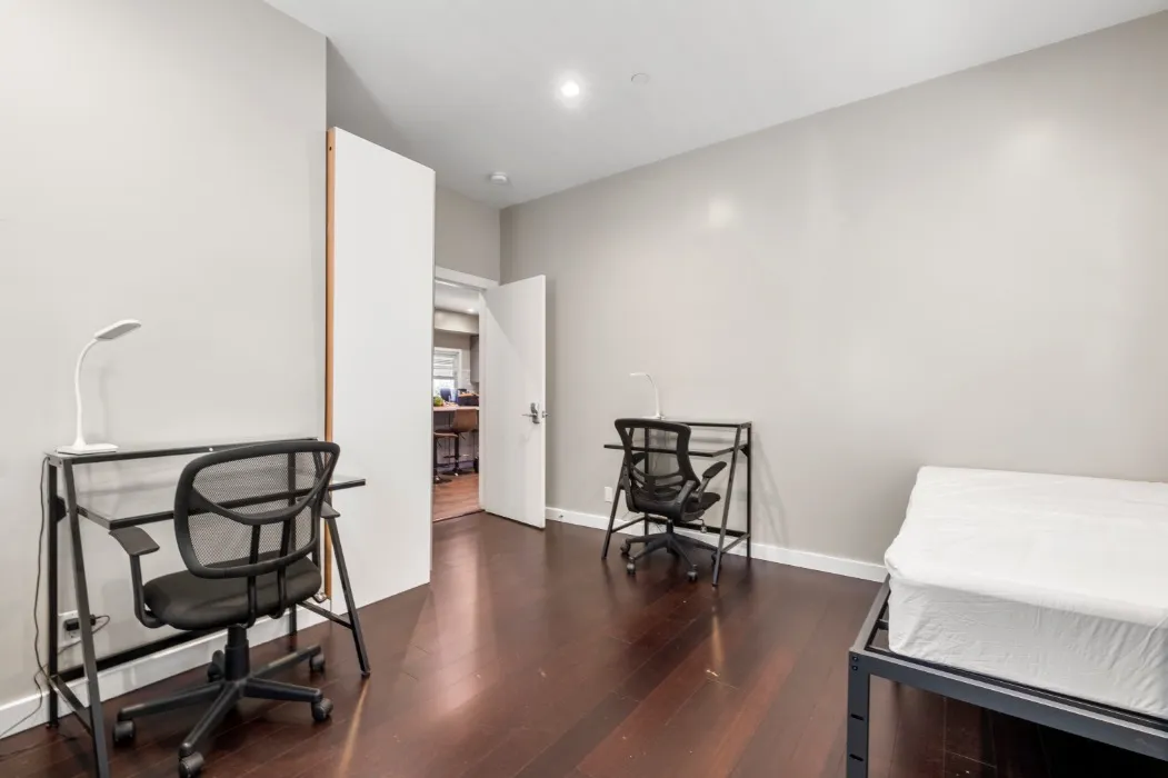Modern bedroom with sleek dark wood flooring, featuring two minimalist study desks and chairs, creating a serene workspace atmosphere.