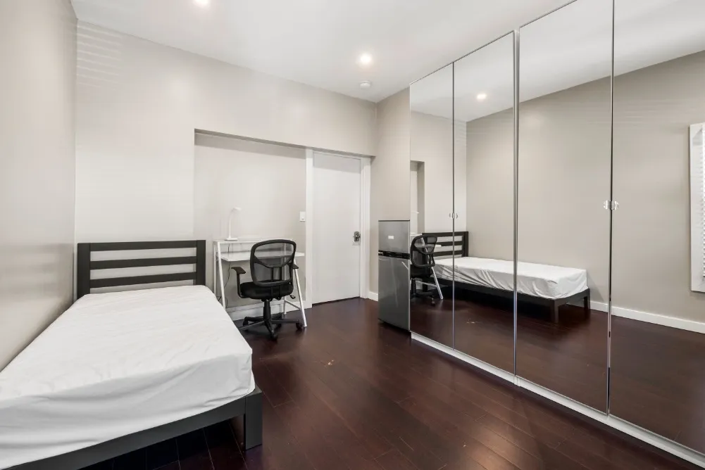 Modern bedroom with sleek mirrored closets, cozy single bed, and functional study area.