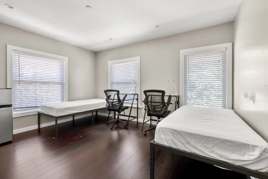 Bright double bedroom with two beds, modern chairs, large windows, and elegant hardwood flooring.